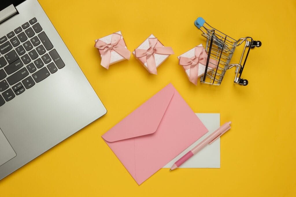 Laptop, koperta z listem i długopisem, pudełka na prezenty i wózek na zakupy na żółtym tle. Boże Narodzenie, walentynki, urodziny. Widok z góry